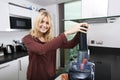 Portrait of young blond woman using juicer for juicing carrots in kitchen