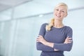 Portrait of a young blonde businesswoman standing with her arms crossed in an office. One cheerful female businessperson Royalty Free Stock Photo