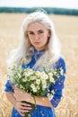 Portrait of a young blonde girl with a bouquet of chamomile in a field