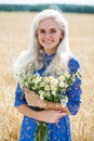 Portrait of a young blonde girl with a bouquet of chamomile in a field