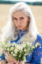 Portrait of a young blonde girl with a bouquet of chamomile in a field