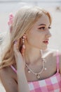 Portrait of young blonde girl looking like a Barbie doll in pink dress, ping bow in her head and jewelry Royalty Free Stock Photo