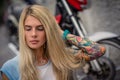 Portrait of a young blonde girl sitting on the background of the motorcycle. Women`s hands with a tattoo. Urban fashion. Royalty Free Stock Photo