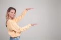 Portrait of young blonde smiling woman with dyed hair woman in yellow sweater shows with hands length of box. Pleased female