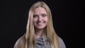 Portrait of young blonde straight-haired model watching smilingly into camera on black background.