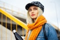 Portrait of young blonde teenager girl, wearing blue denim jacket, with orange scarf and plaid cap, holding a black steel bottle. Royalty Free Stock Photo