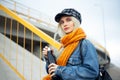 Portrait of young blonde teenager girl, wearing denim jacket, with orange scarf and plaid cap, holding a black steel eco bottle. Royalty Free Stock Photo