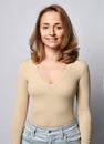 Portrait of young blonde woman in beige shirt, bodysuit with long sleeves and jeans with open friendly smile