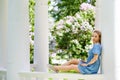 Portrait of a young blonde woman in a blue dress in a blooming lilac park near a white gazebo. Spring blooming on a sunny day