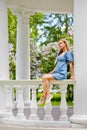 Portrait of a young blonde woman in a blue dress in a blooming lilac park near a white gazebo. Spring blooming on a sunny day