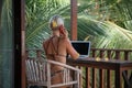 Portrait of young blonde woman freelancer working with laptop on balcony of tropical bungalow with palm trees view Royalty Free Stock Photo