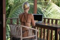 Portrait of young blonde woman freelancer working with laptop on balcony of tropical bungalow with palm trees view Royalty Free Stock Photo