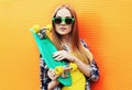 Portrait young blonde woman with green skateboard wearing a sunglasses over colorful orange wall Royalty Free Stock Photo