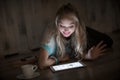 Portrait of young blonde woman looks and reads on tablet and drinking coffee at night. girl uses the tablet