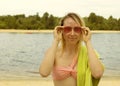 Portrait of a young blonde woman in red glasses with a towel near the river. Girl resting Royalty Free Stock Photo