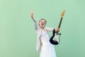 Portrait of young blonde woman in white shirt, skirt, and striped blouse and electric guitar standing with rock sign tongue out Royalty Free Stock Photo