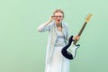 Portrait of young blonde woman in white shirt and striped blouse, electric guitar standing, holding eyeglasses and looking Royalty Free Stock Photo