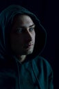 Portrait of a young blue-eyed man with a hood covering his head who in the shadow is staring away