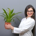 Portrait of young botanist woman in uniform holding plant against gray background