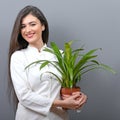 Portrait of young botanist woman in uniform holding plant against gray background