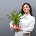 Portrait of young botanist woman in uniform holding plant against gray background Royalty Free Stock Photo