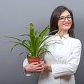 Portrait of young botanist woman in uniform holding plant against gray background