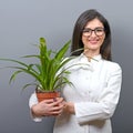 Portrait of young botanist woman in uniform holding plant against gray background Royalty Free Stock Photo