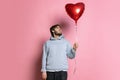 Portrait of young boy holding red balloon in heart shape isolated over pink background. Valentine's Day Royalty Free Stock Photo