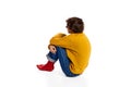 Portrait of young boy sitting on floor in depression, hugging legs over white background. Feeling lonely, sad. Introvert