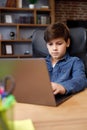 Portrait of young boy studying remotely at home using laptop. Cute schoolboy doing homework, looking at computer screen Royalty Free Stock Photo