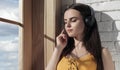 Portrait of young brunette girl listening to music while sitting on window sill Royalty Free Stock Photo