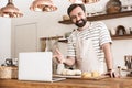 Portrait of young brunette man using laptop while making homemade pasta in kitchen at home Royalty Free Stock Photo