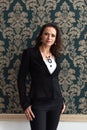 Portrait of a young brunette woman in a black business suit standing near a vintage wall with her hands in her pockets and smiling Royalty Free Stock Photo