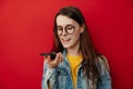 Portrait of young brunette woman in eyeglasses holding phone speak activate virtual digital voice assistant on smartphone Royalty Free Stock Photo