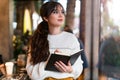 Portrait of young brunette woman standing in cafe, writing in notebook, looking out window. Girl makes notes in diary, plans Royalty Free Stock Photo