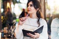 Portrait of young brunette woman standing in cafe, writing in notebook, looking out window. Girl makes notes in diary, plans Royalty Free Stock Photo