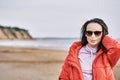 Portrait of a young brunette woman in sunglasses and a red jacket. Woman on a walk along the sandy shore of a large river on a spr