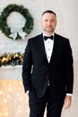 Portrait of a young business man in black suit and bow tie smiling at the camera while holding one hand in his pocket on christmas Royalty Free Stock Photo