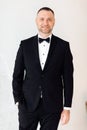 Portrait of a young business man in black suit and bow tie smiling at the camera while holding one hand in his pocket on white Royalty Free Stock Photo