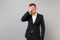 Portrait of young business man in classic black suit, shirt covering eyes, face with hand isolated on grey wall Royalty Free Stock Photo