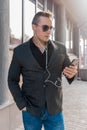 Portrait of a young business man in sunglasses, jacket and shirt with jeans and headphones listening to music from a mobile phone Royalty Free Stock Photo