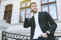 Portrait of young business man using mobile phone on building outdoors. Cheerful handsome caucasian man in black suit in the city Royalty Free Stock Photo
