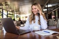 Portrait of young woman sitting in cafe in front of her laptop and talking on mobile phone Royalty Free Stock Photo