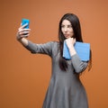 Portrait of a young business woman in grey dress with blue smartphone and a tablet making a selfie and looking on the phone