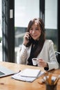 Portrait of young business woman sitting in front of her laptop and talking on mobile phone. Royalty Free Stock Photo