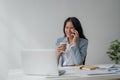 Portrait of young business woman with sitting in office in front of her laptop and talking on mobile phone hand holding Royalty Free Stock Photo