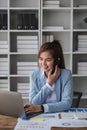 Portrait of young business woman with sitting in office in front of her laptop and talking on mobile phone hand at Royalty Free Stock Photo