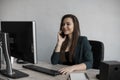 Portrait of young business woman talking phone against computer screen in white office. Female entrepreneur having call Royalty Free Stock Photo