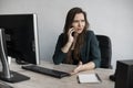 Portrait of young business woman talking phone against computer screen in white office. Female entrepreneur having call Royalty Free Stock Photo