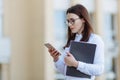 Portrait young business woman wearing white shirt using smartphone out doors. Female reading sms message in working Royalty Free Stock Photo